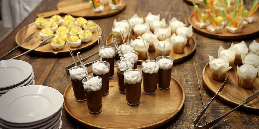 A few trays of party snacks laid out on a large wooden table. Some of the treats are topped with white whipped cream, resembling snow.
