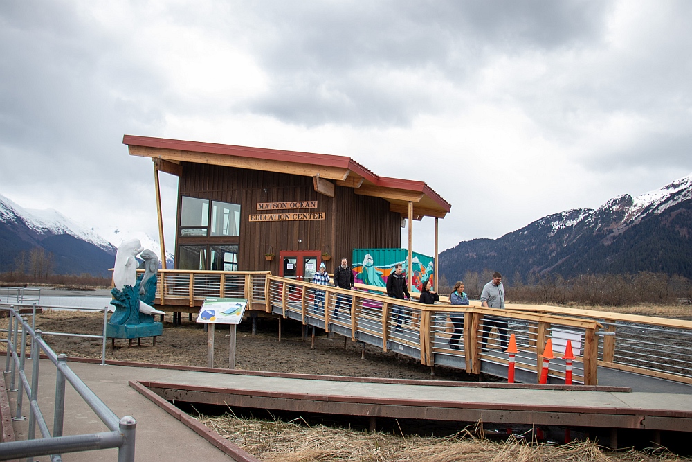 Boardwalk leads to new Matson Ocean Education Center. Mountains and a cloudy sky in the background.