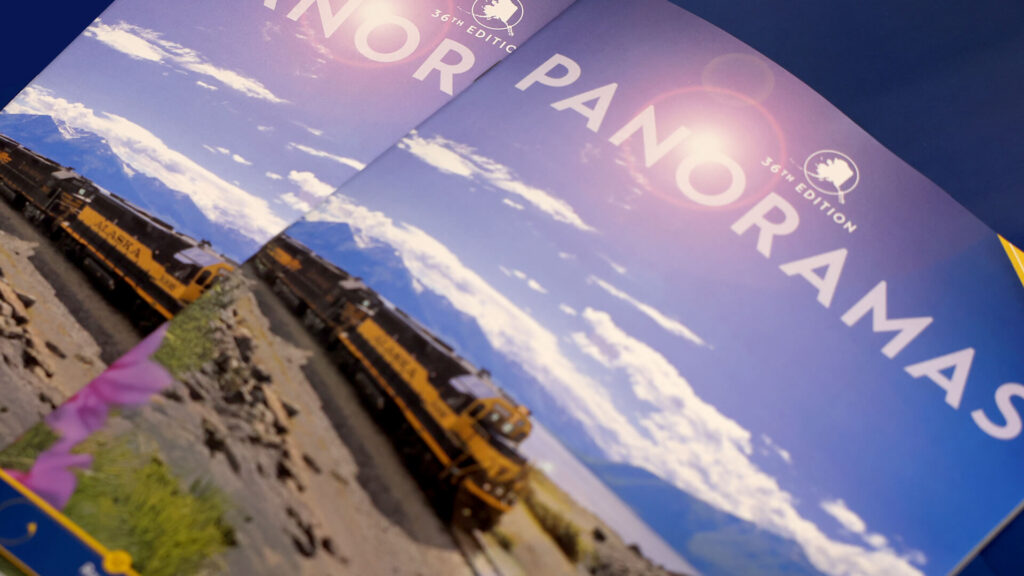 Brochures with a train and mountain landscape on the cover, titled “PANORAMAS 36th Edition,” are shown overlapping against a blue background.